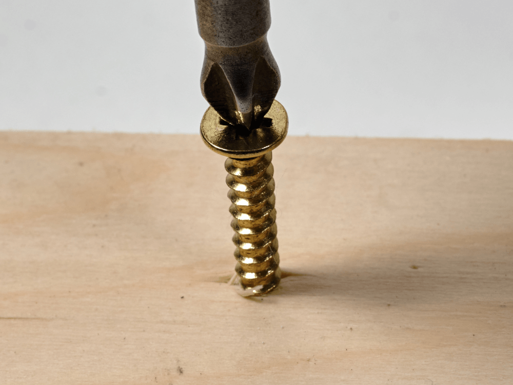 Parafuso dourado sendo apertado com uma ponta de ferramenta, mostrando o encaixe entre a ferramenta e a cabeça do parafuso.