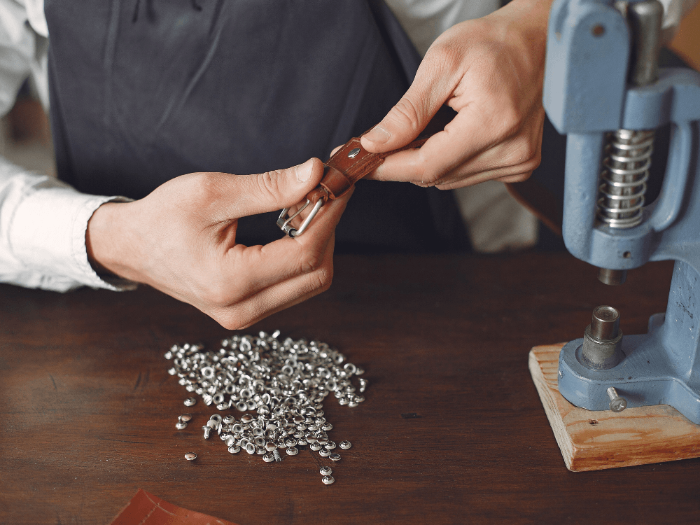 Profissional manuseia uma ferramenta de aplicação de tipos de rebites metálicos ao lado de uma prensa utilizada na fixação de componentes.